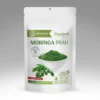 Moringa prah u beloj kesici sa zelenim prahom i svežim listovima moringe