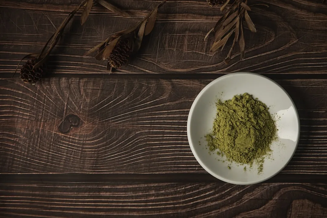 Posuda s moringa prahom na tamnom drvenom stolu pored sušenog bilja