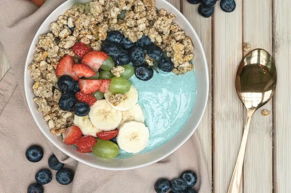 Smoothie bowl sa plavim jogurtom, granolom, jagodama, borovnicama, bananom i grožđem na drvenom stolu