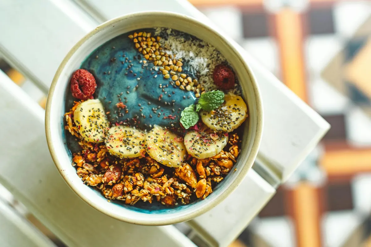 Smoothie bowl sa plavim kremom, granolom, bananom, malinama i chia semenkama u keramičkoj posudi