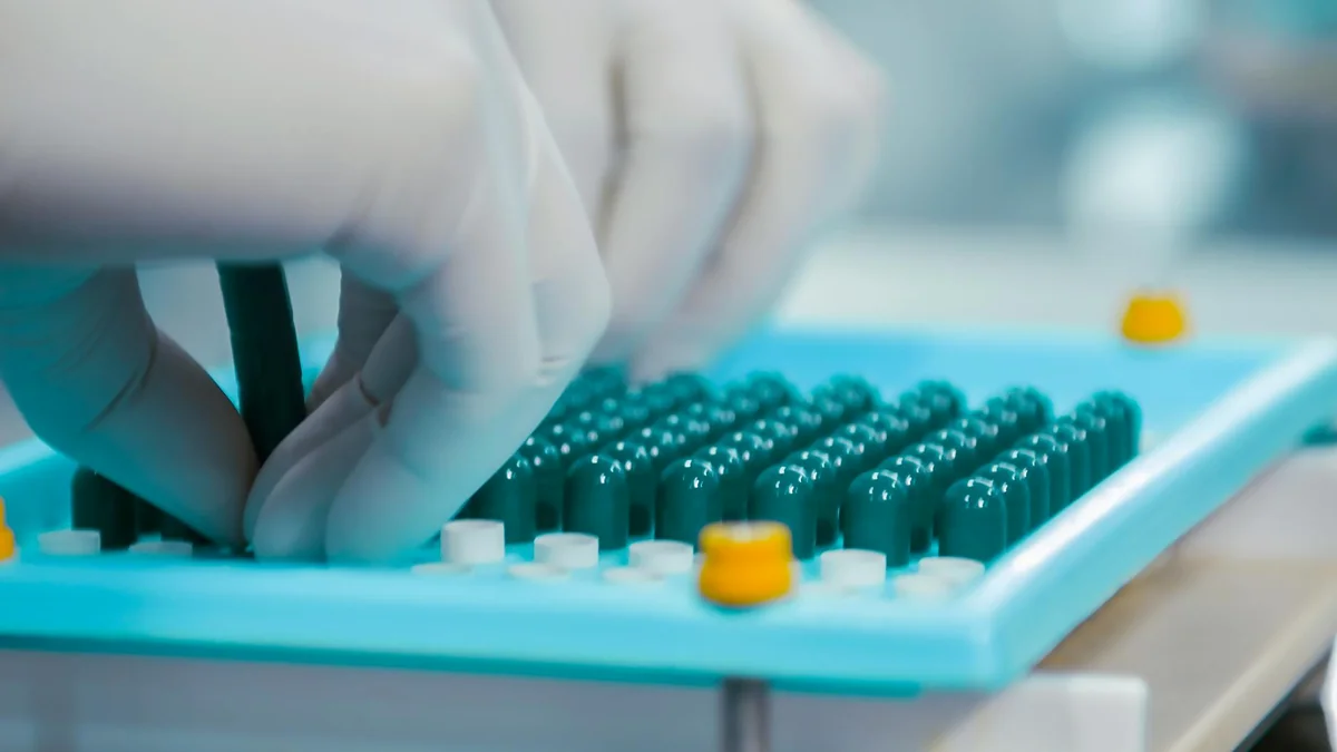 Ruke u zaštitnim rukavicama sortiraju zelene kapsule na farmaceutskom pladnju u laboratorijskom osvetljenju