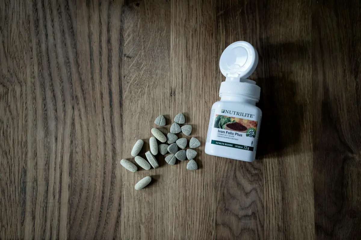 Zelene tablete Nutrilite suplemenata rasute pored bele bočice na tamnoj drvenoj podlozi