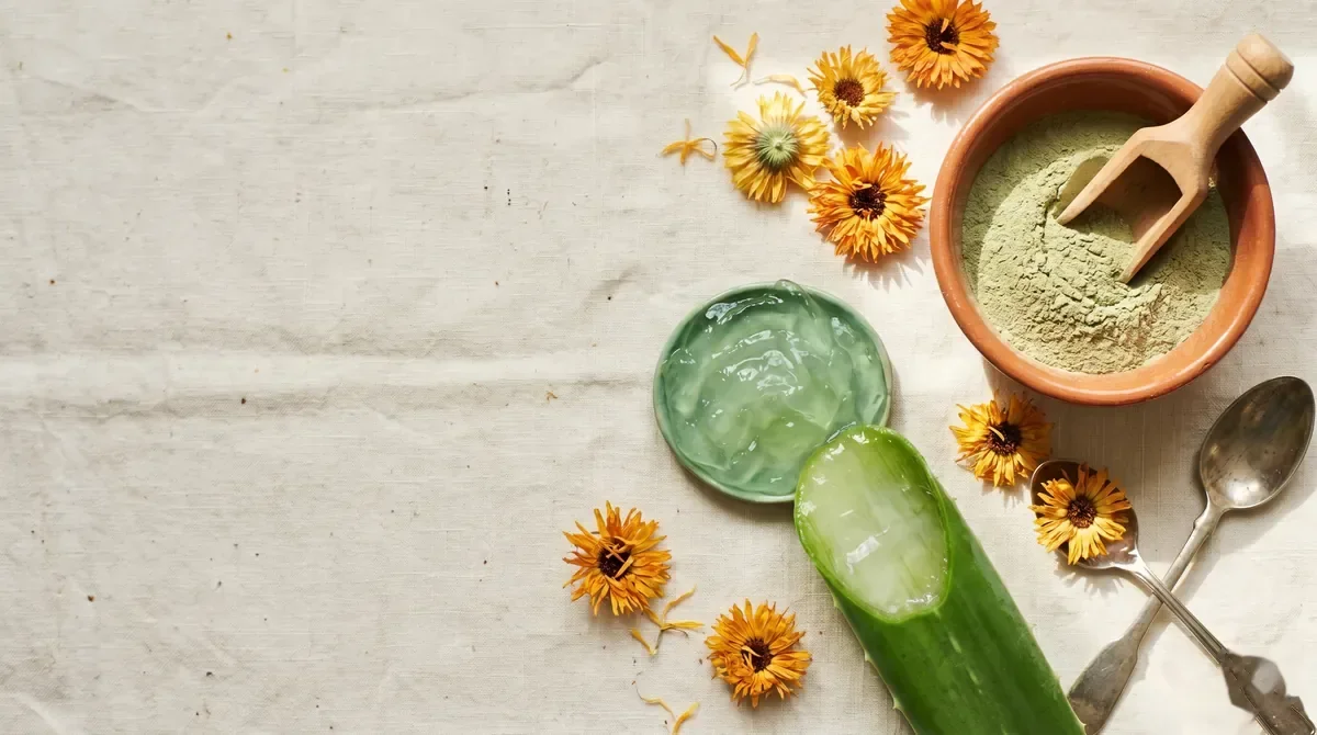 Prirodni sastojci za negu kože sklone aknama - čajno drvo, aloe vera gel i neven na drvenom stolu