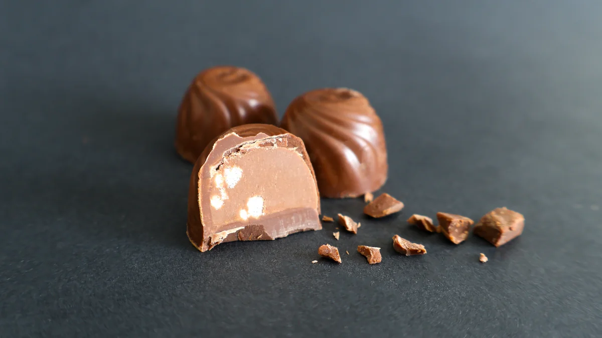 Čokoladne praline na tamnoj podlozi, jedna presečena, sa mrvicama čokolade oko njih