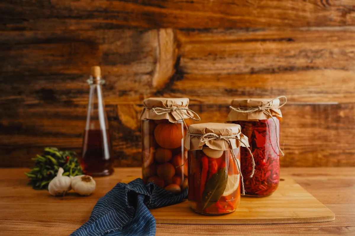 Fermentisano povrće u teglama sa paradajzom i paprikom, beli luk i začinsko bilje na drvenoj podlozi.